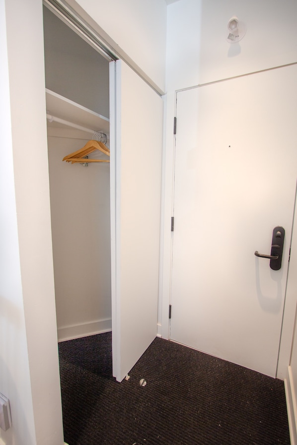 A narrow hallway with a white door on the right and a closet with a wooden hanger on the left. - Unique Stays - 4119 St-Denis (Montreal)