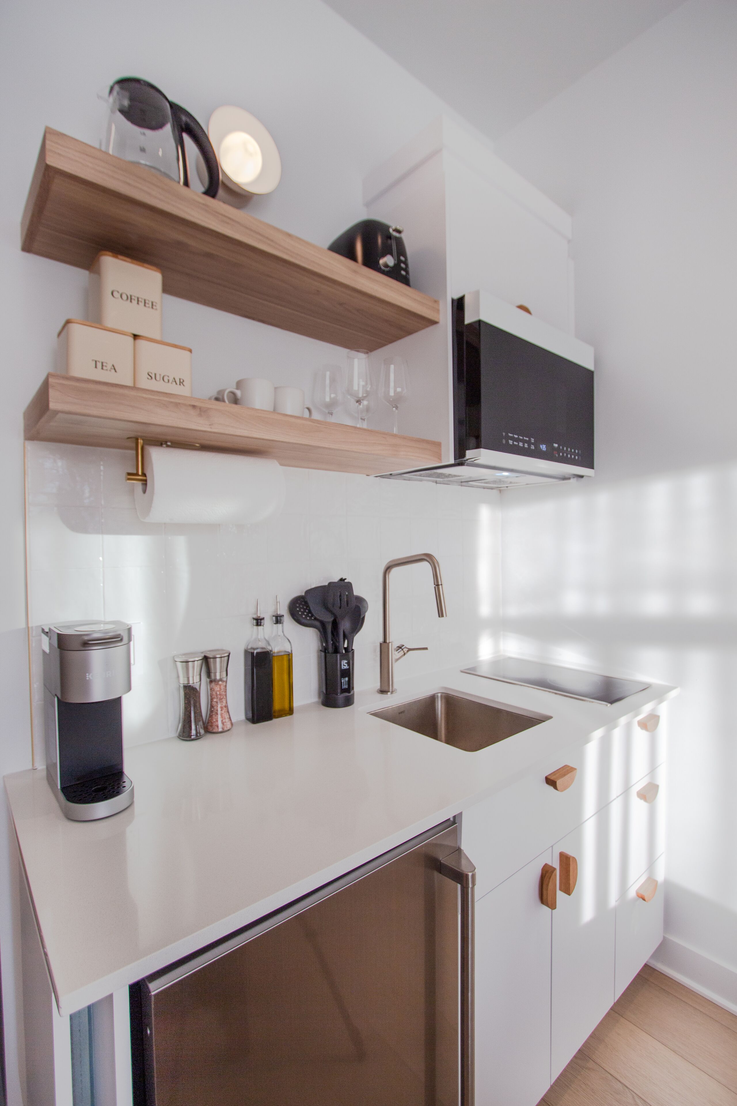 A modern kitchen with a built-in dishwasher, stainless steel sink, and wooden shelves above the counter.