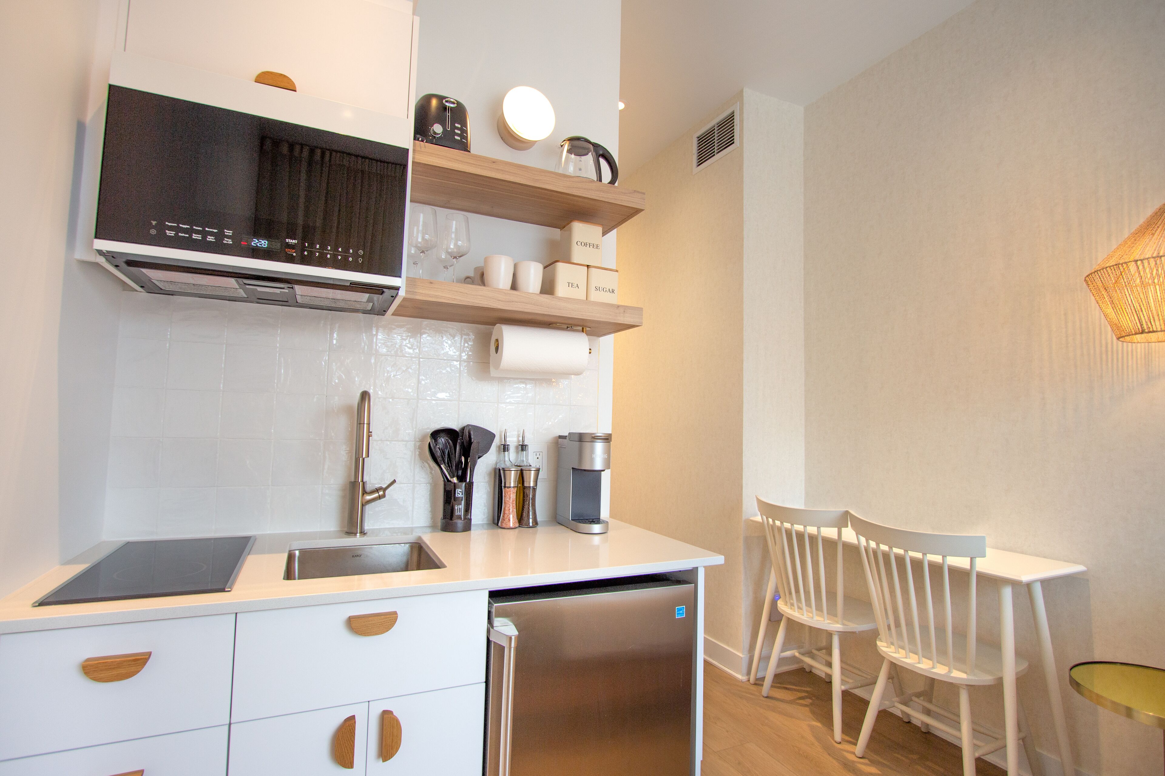 A modern kitchen with a built-in dishwasher, a coffee machine, and a set of white chairs at a small table.