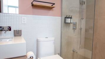 Un baño moderno con inodoro, lavabo y ducha con mampara de vidrio.