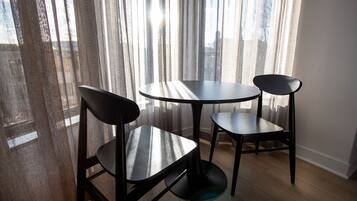 A room with two round tables and two chairs, large windows with sheer curtains, and wooden flooring.