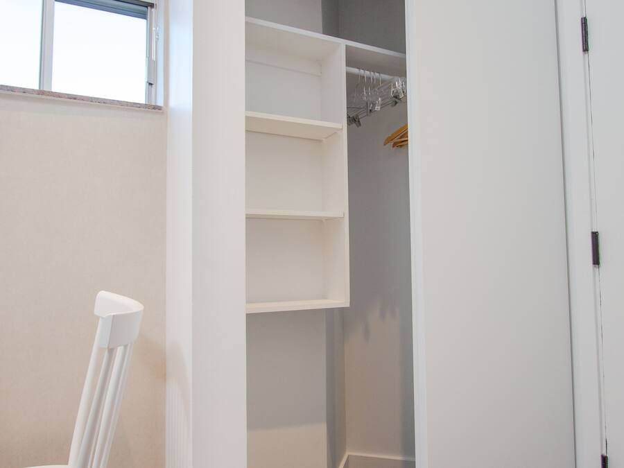A room with a white chair, a closet with shelves, and a window.
