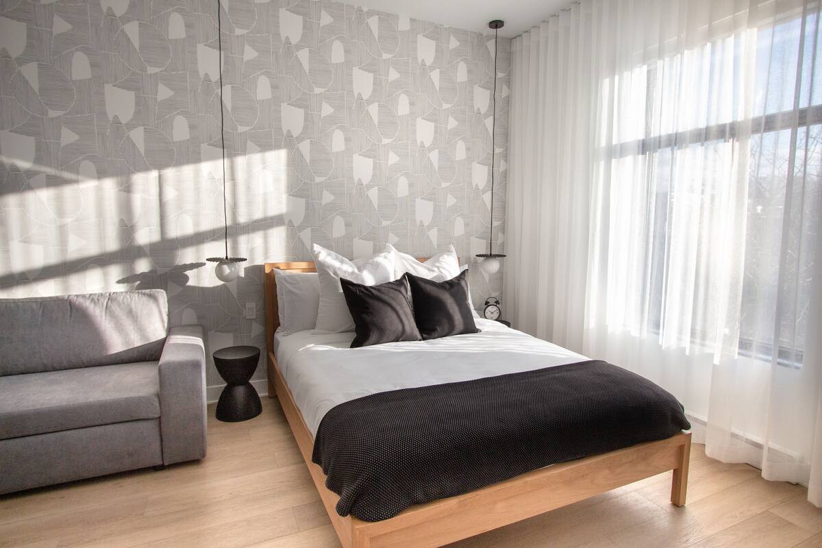 A modern bedroom with a bed, a grey sofa, and a bedside table.