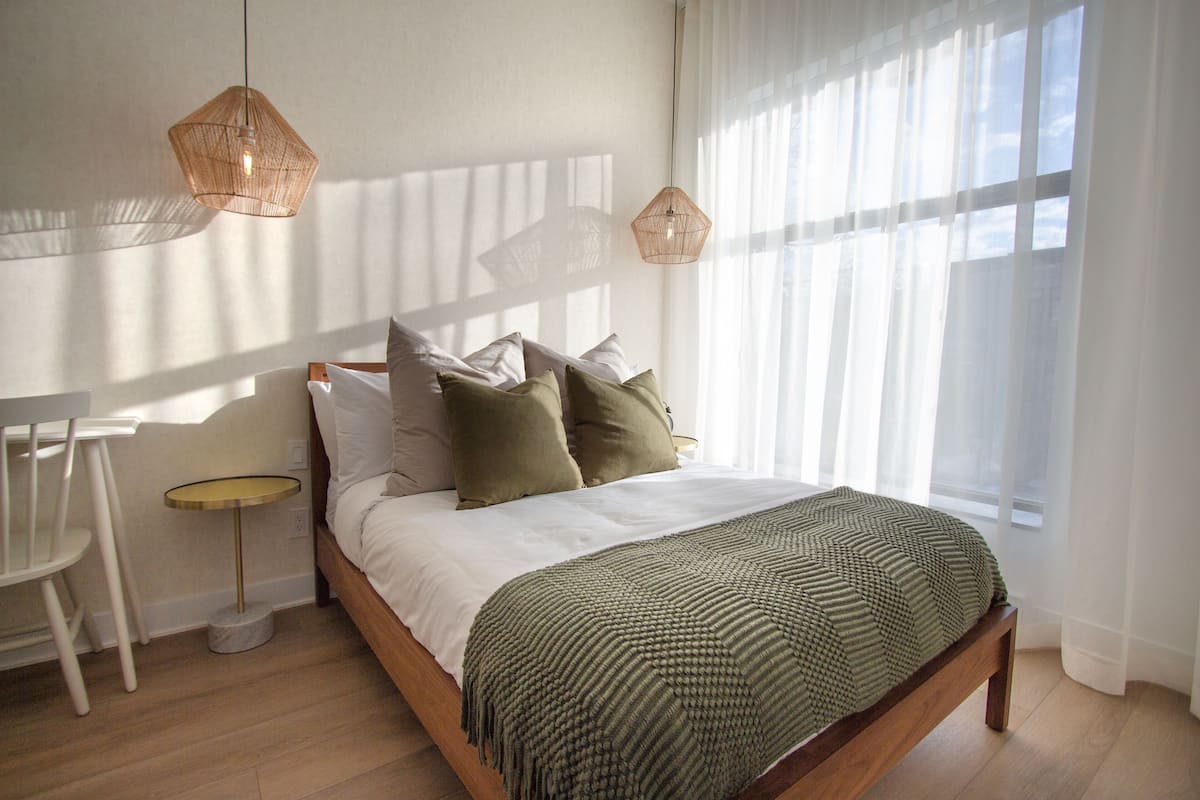 A neatly made bed with a green patterned blanket, a bedside table, and two hanging light fixtures.