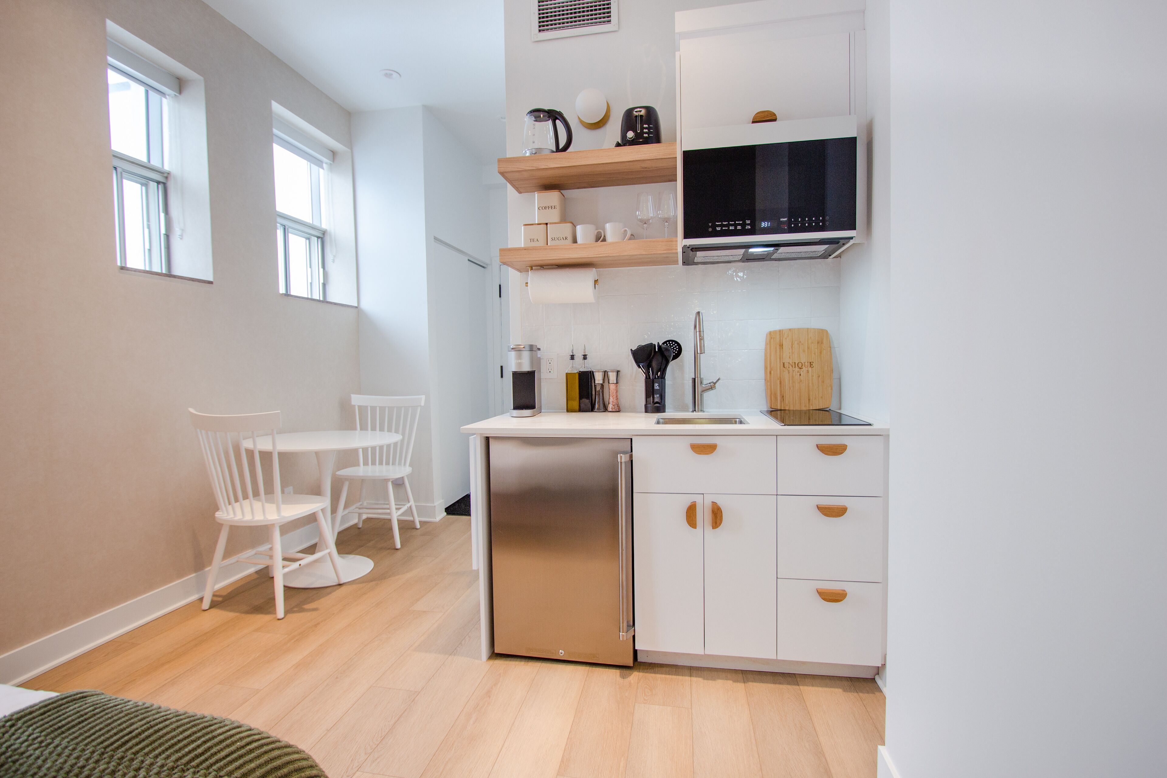 A modern kitchen with white cabinetry, a built-in dishwasher, and a microwave. There is a dining area with a white table and chairs.
