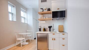A modern kitchen with white cabinetry, a built-in dishwasher, and a microwave. There is a dining area with a white table and chairs.