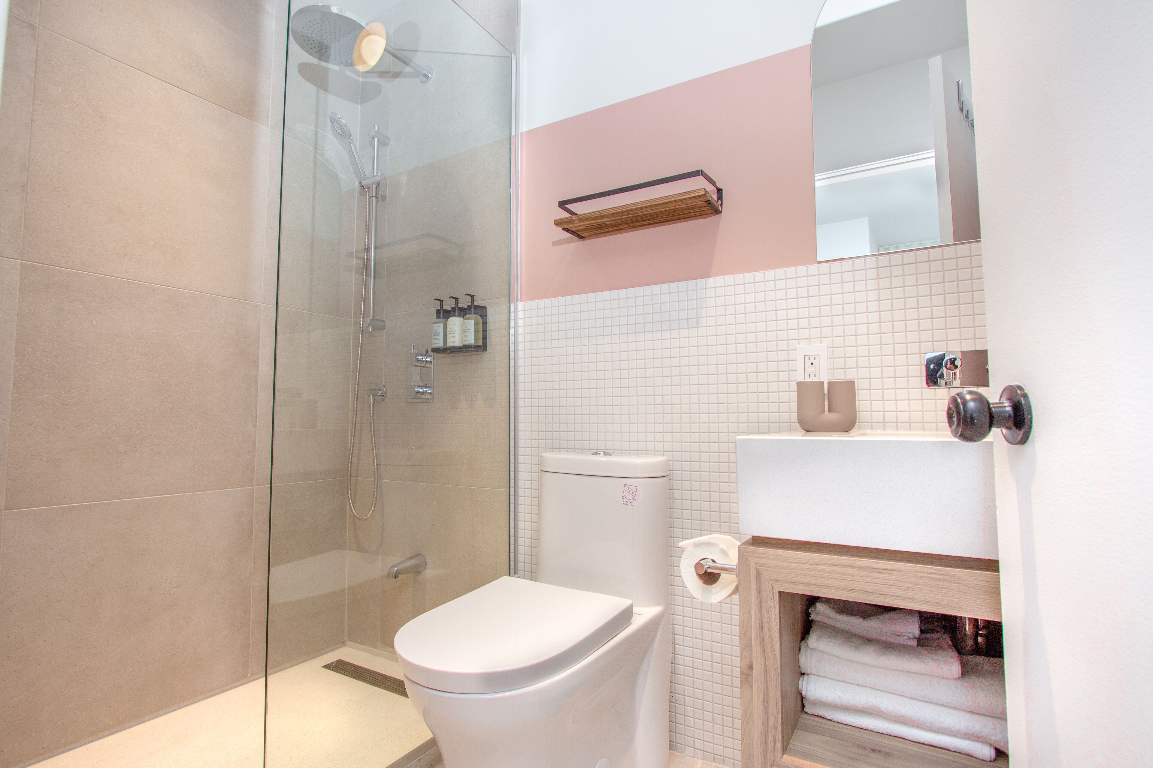 Une salle de bain moderne avec une douche à l’italienne en verre, des toilettes blanches et un meuble-lavabo en bois avec un miroir.