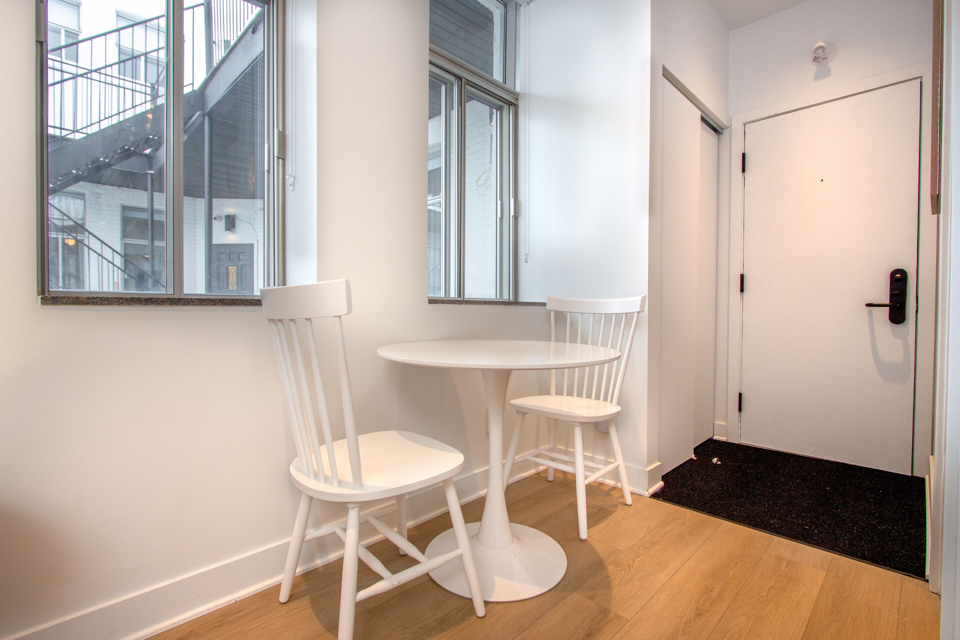 A small, white, round table with two matching chairs in a corner of a room with wooden flooring and white walls.