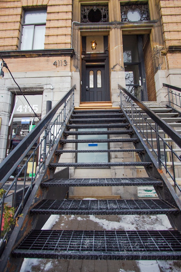 A set of metal stairs leading to a building entrance with a black door and a small light above it. - Unique Stays - 4119 St-Denis (Montreal)
