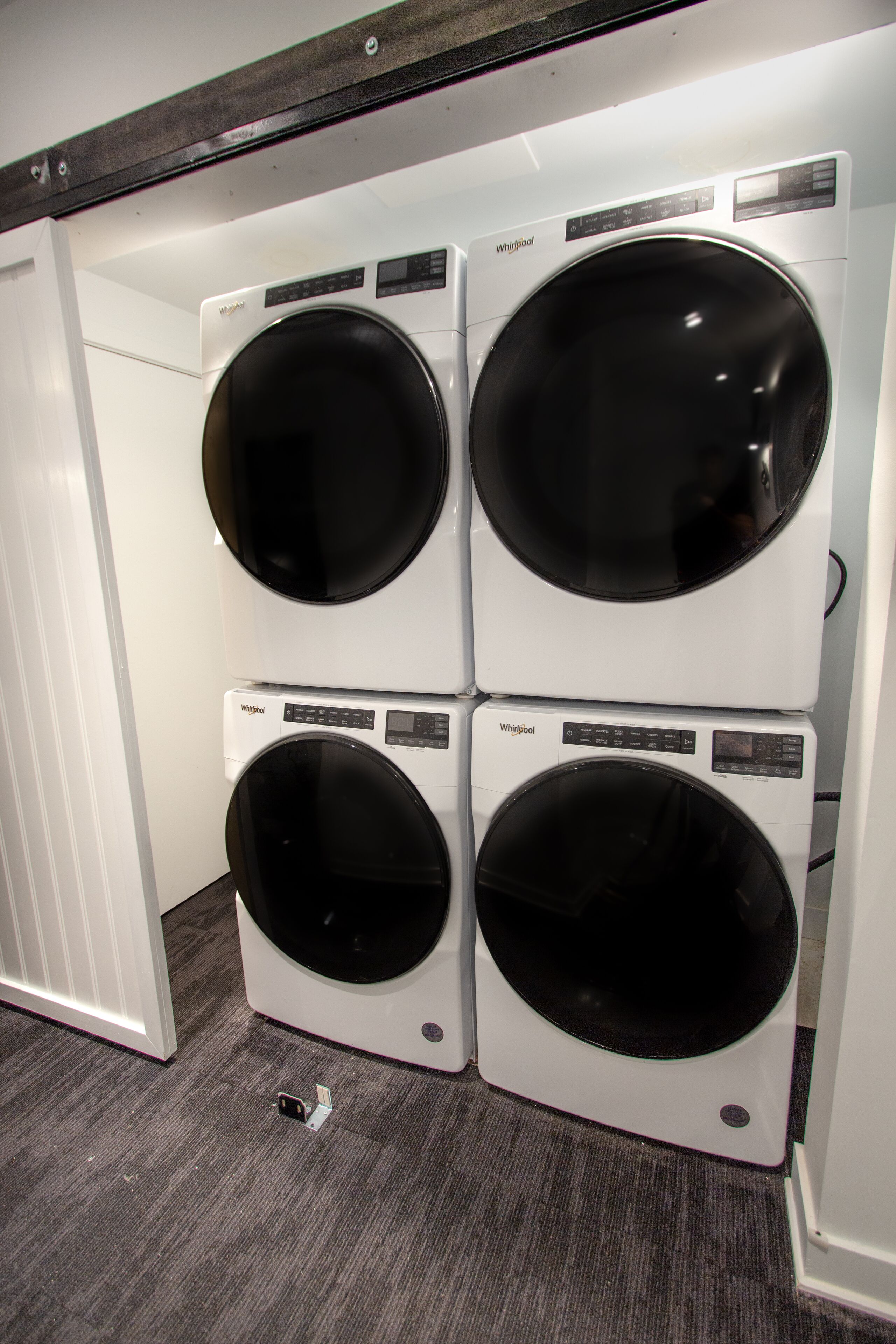 Une buanderie équipée de quatre machines à laver Whirlpool à chargement frontal, disposées les unes sur les autres.