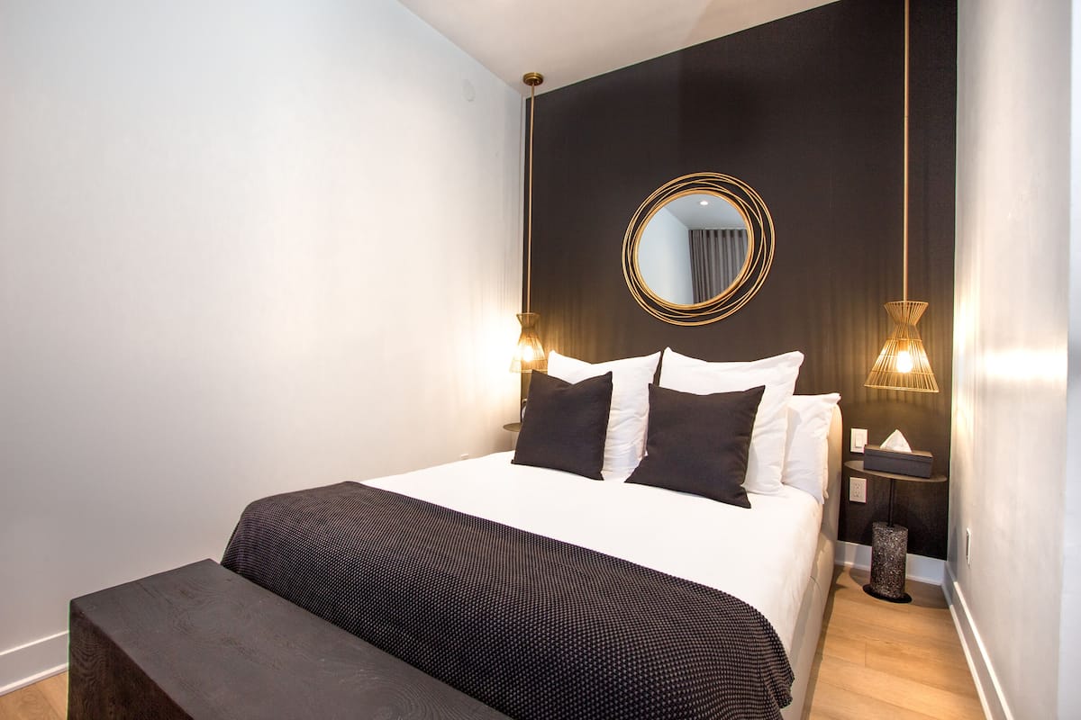 A modern hotel room with a large bed, a round mirror, and two wall-mounted lamps.