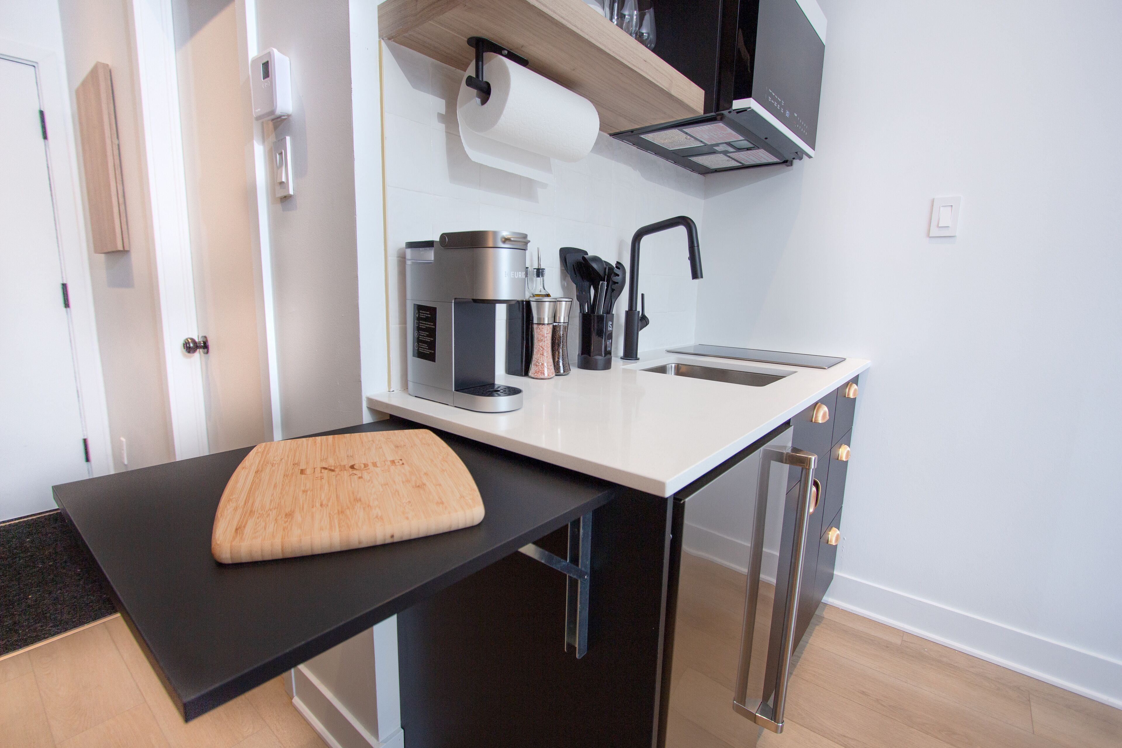 A modern kitchen with a black countertop, a wooden cutting board, a coffee maker, and a sink.