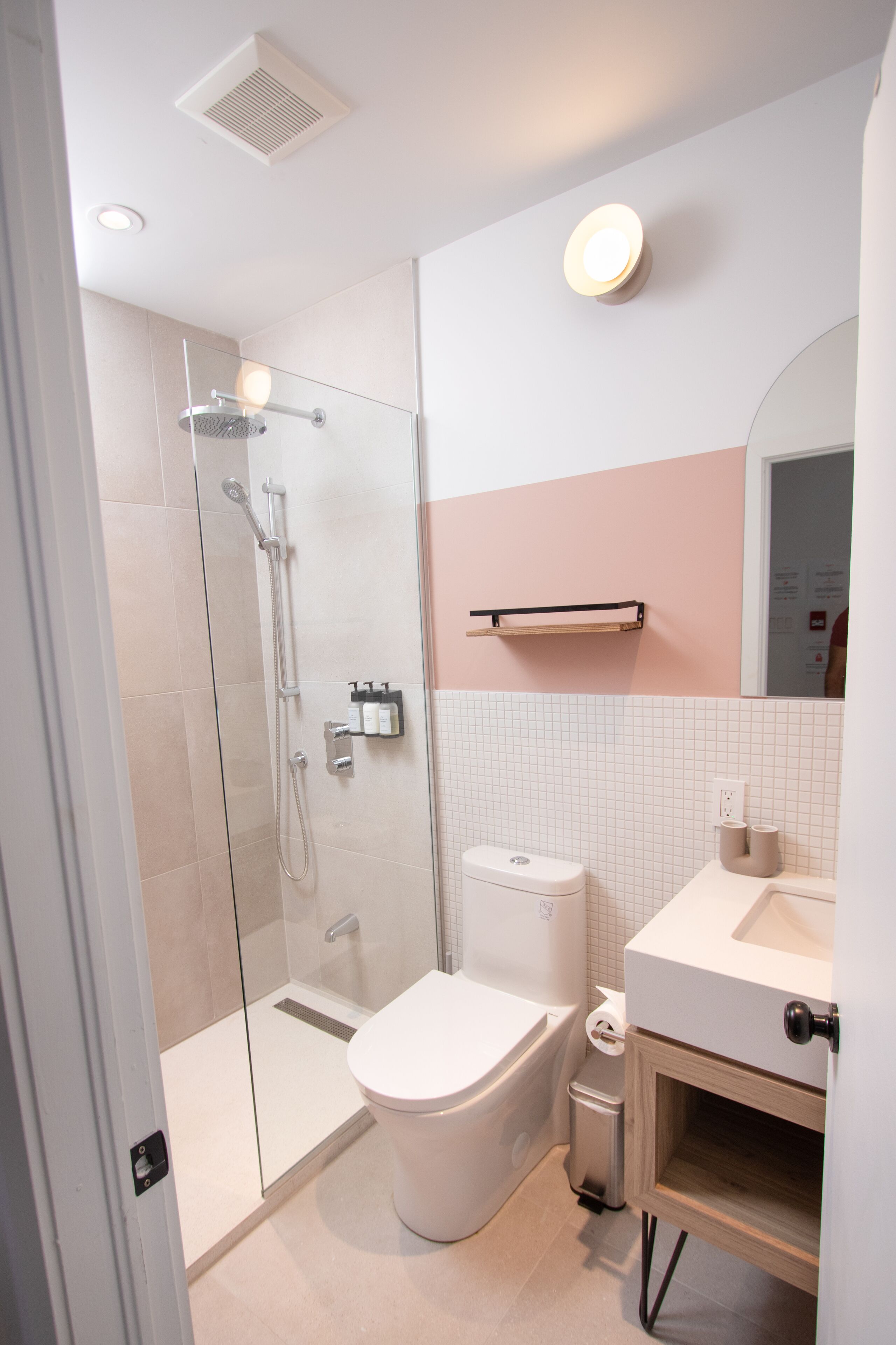 Un baño moderno con ducha de vidrio, inodoro blanco y lavamanos con espejo.