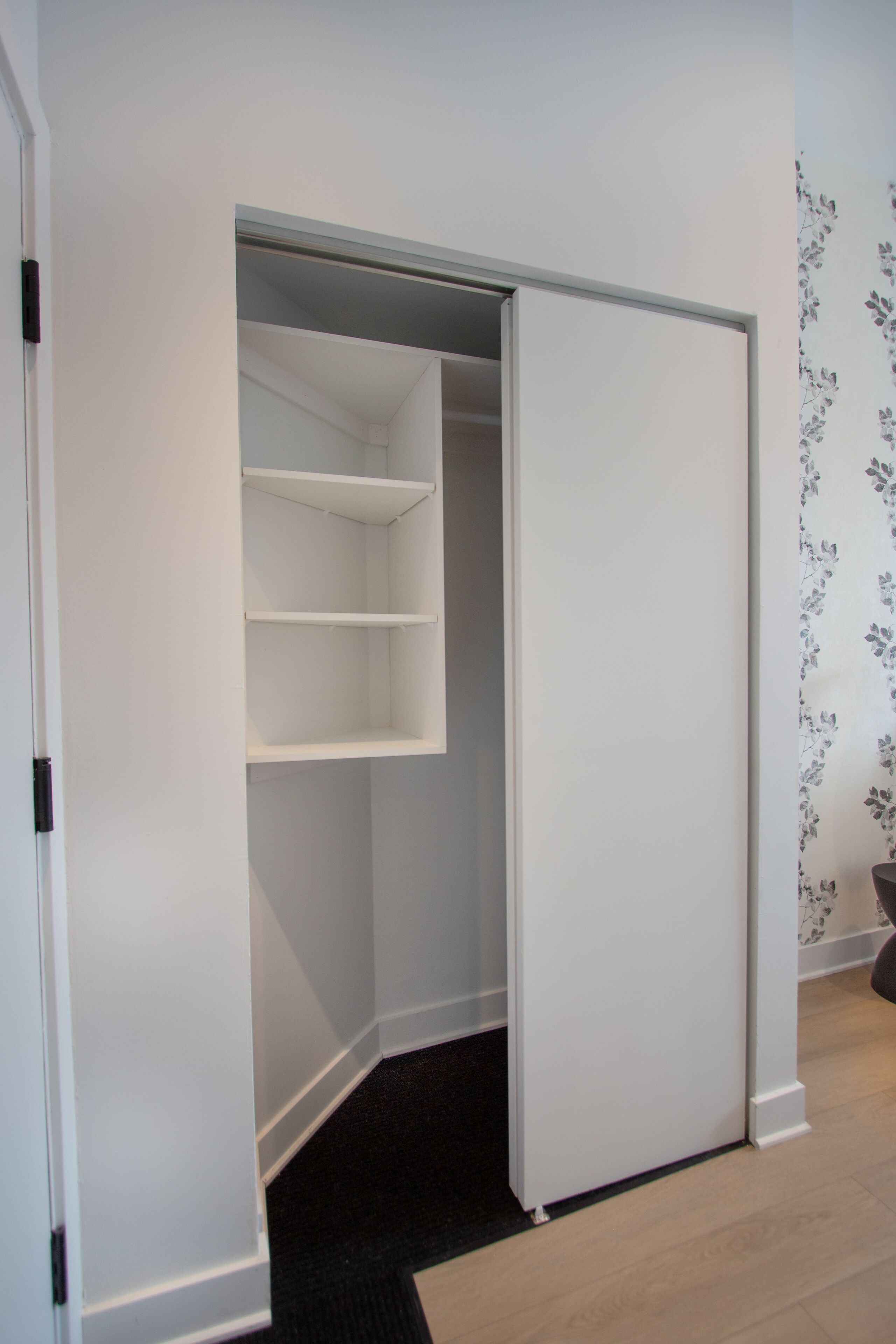 Ein begehbarer Kleiderschrank mit offenen Türen, der Regale und einen schwarzen Teppichboden zeigt.