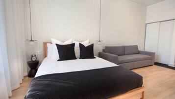 Un dormitorio moderno con una cama grande, un sofá gris y un banco de madera.