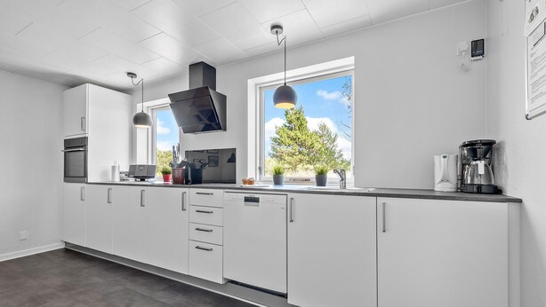 A modern kitchen with white cabinets, a built-in oven, a coffee maker, and a window with a view of trees.