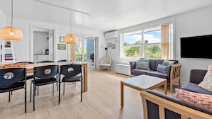 A modern living room with a dining area, large windows, and a flat-screen TV.