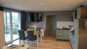 A modern kitchen with a dining area, wooden flooring, and a view to the outside. - Aparthotel Rotheul (Föritztal)