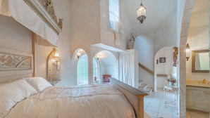 Un dormitorio con una cama grande, un tocador con espejo y una escalera que lleva a un nivel superior.