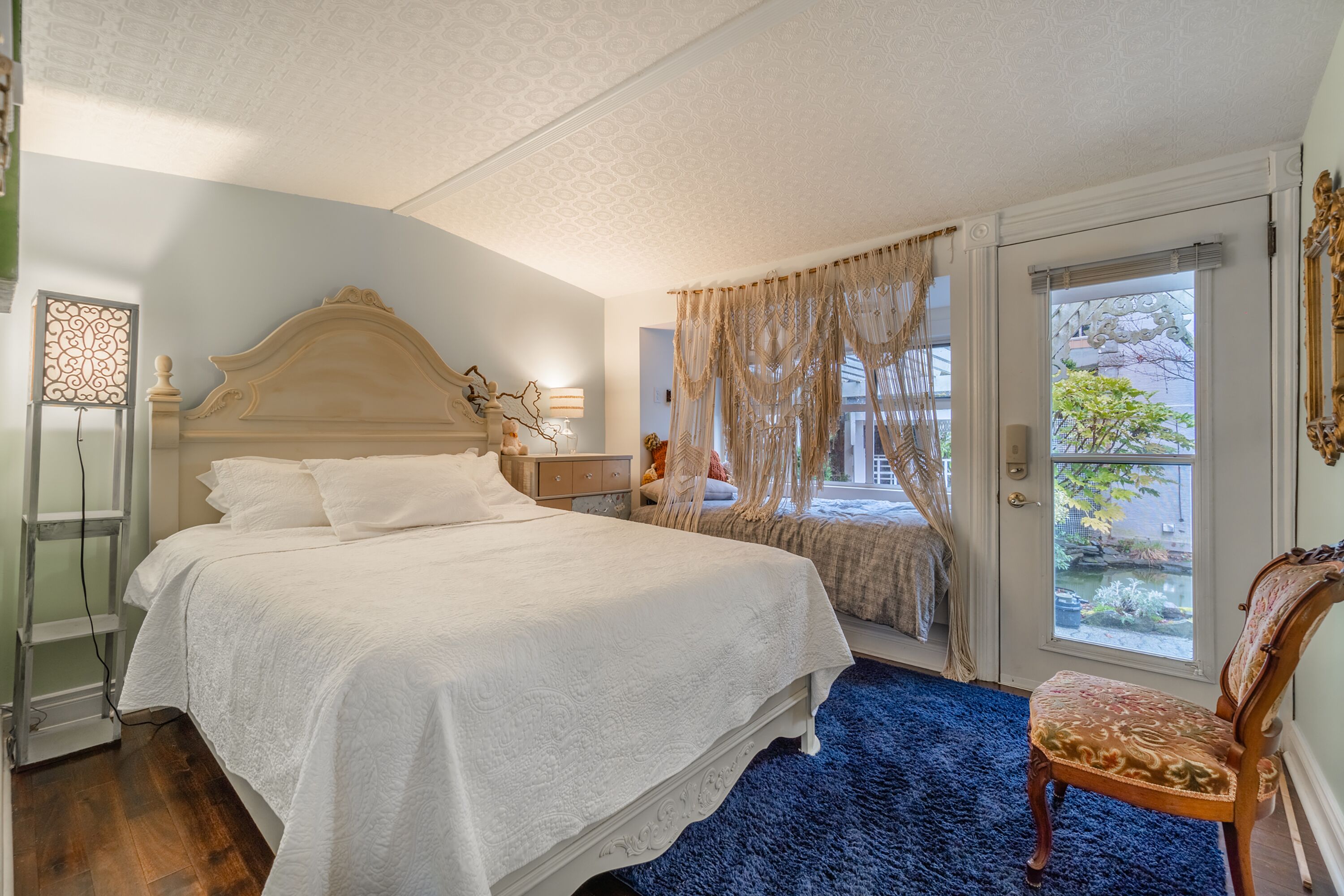 Un dormitorio con una cama grande, una silla, una ventana con cortinas y vistas al exterior.