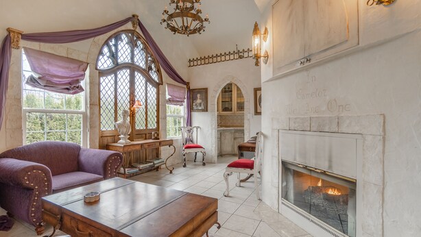 Una habitación con chimenea, una mesa de madera, un sofá morado y una ventana con vista a la vegetación.