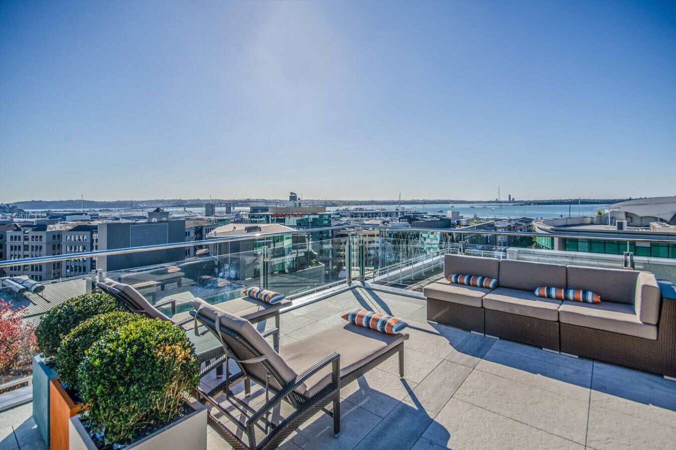 A rooftop terrace with outdoor seating, a glass balustrade, and a city view.
