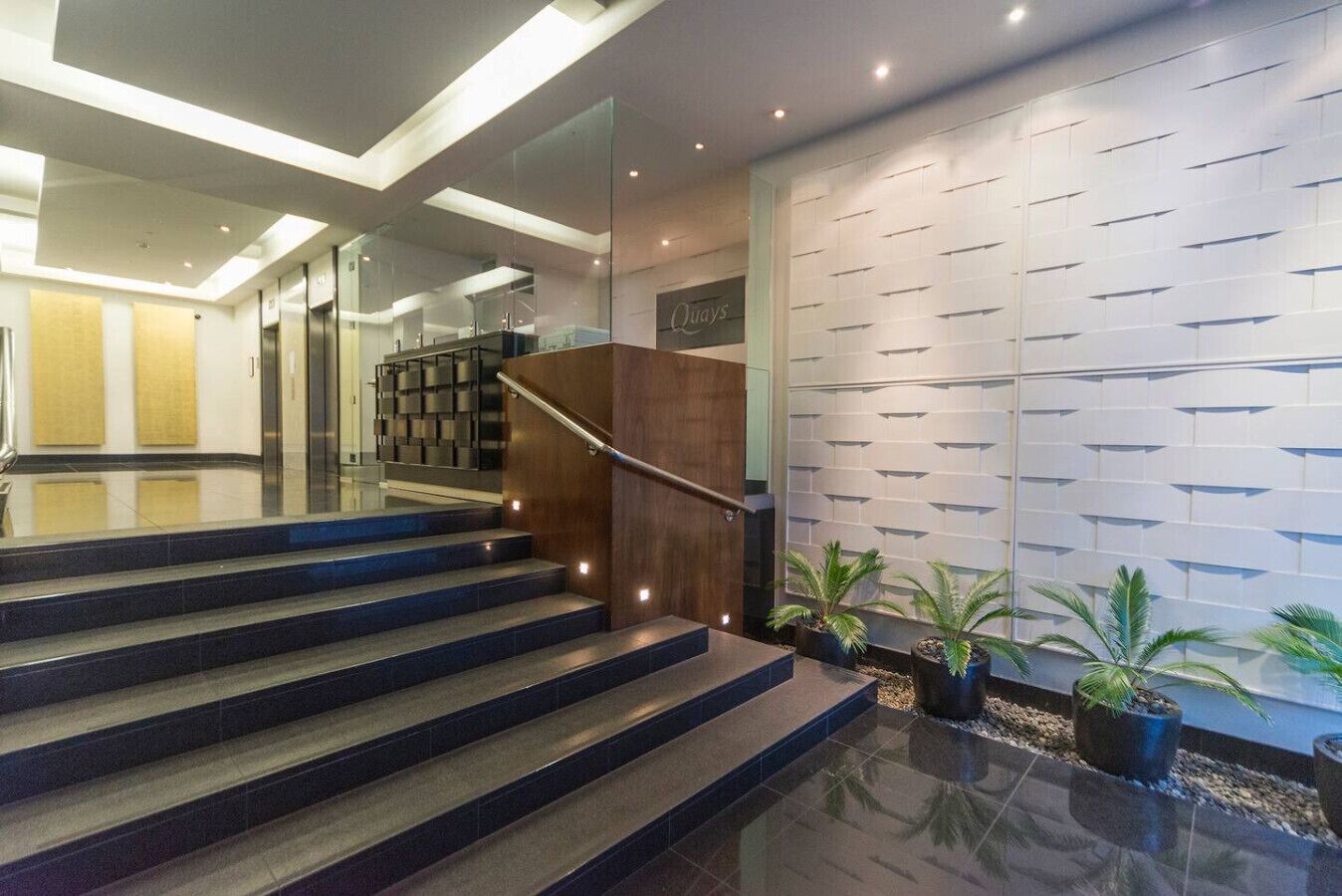 A modern hotel lobby with a staircase, a reception desk, and a wall with a geometric pattern.