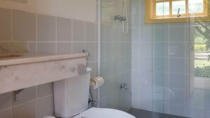 Une salle de bain comprenant des toilettes, une poubelle, un espace douche et une fenêtre.