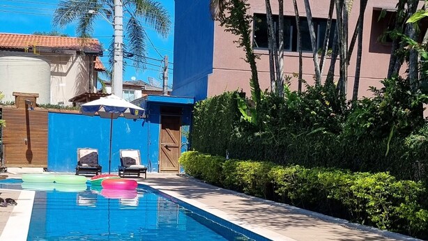 Une piscine dotée de chaises longues et d’un parasol, entourée de palmiers et d’un bâtiment.