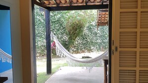 Une porte qui donne sur un jardin aménagé avec un hamac, un chemin en béton et un plafond carrelé.
