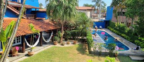 A pool area with a clear view of the surrounding buildings, including a blue house with a tiled roof and a hammock.