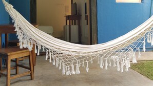 Un hamac dans une pièce aux murs bleus, avec une chaise en bois et une petite fenêtre.