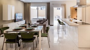 Een moderne hotelkamer met een eethoek, een bank, een televisie en een keukenhoek.