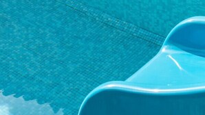 Ein klares, blaues Schwimmbecken mit einem blauen Liegestuhl und einem Abdeckrost.