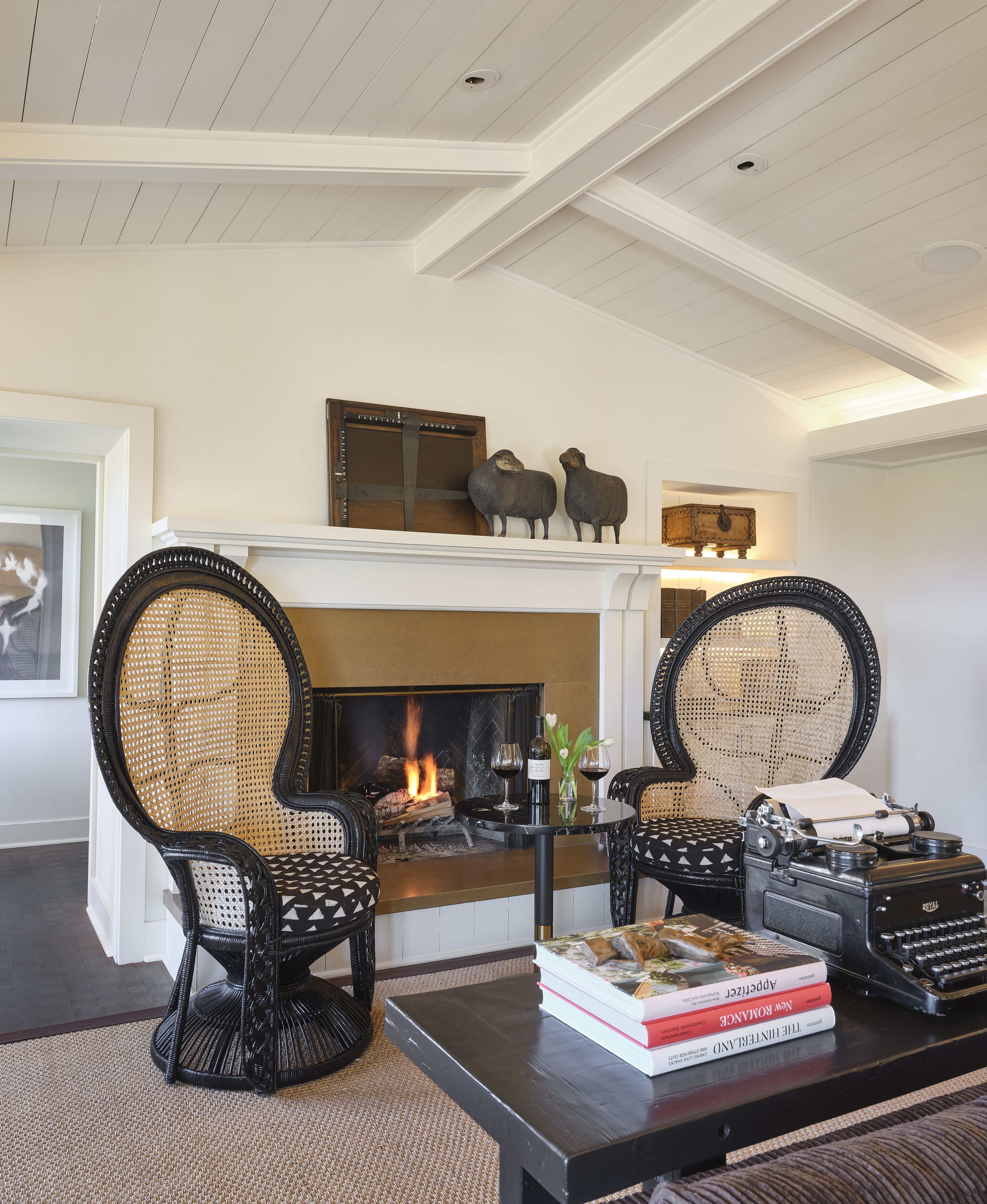 A living room with a fireplace, two black wicker chairs, a coffee table, and a typewriter.