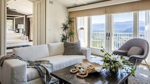 A modern hotel room with a sofa, armchair, and a view of the mountains through large windows. - Sttupa Estate Napa Valley (Napa)