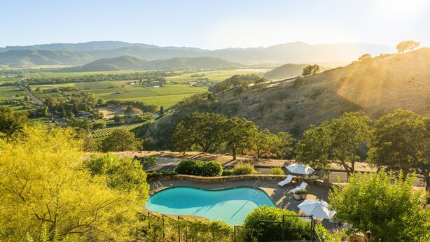 A pool with lounge chairs and umbrellas, surrounded by trees and hills. - Sttupa Estate Napa Valley (Napa)
