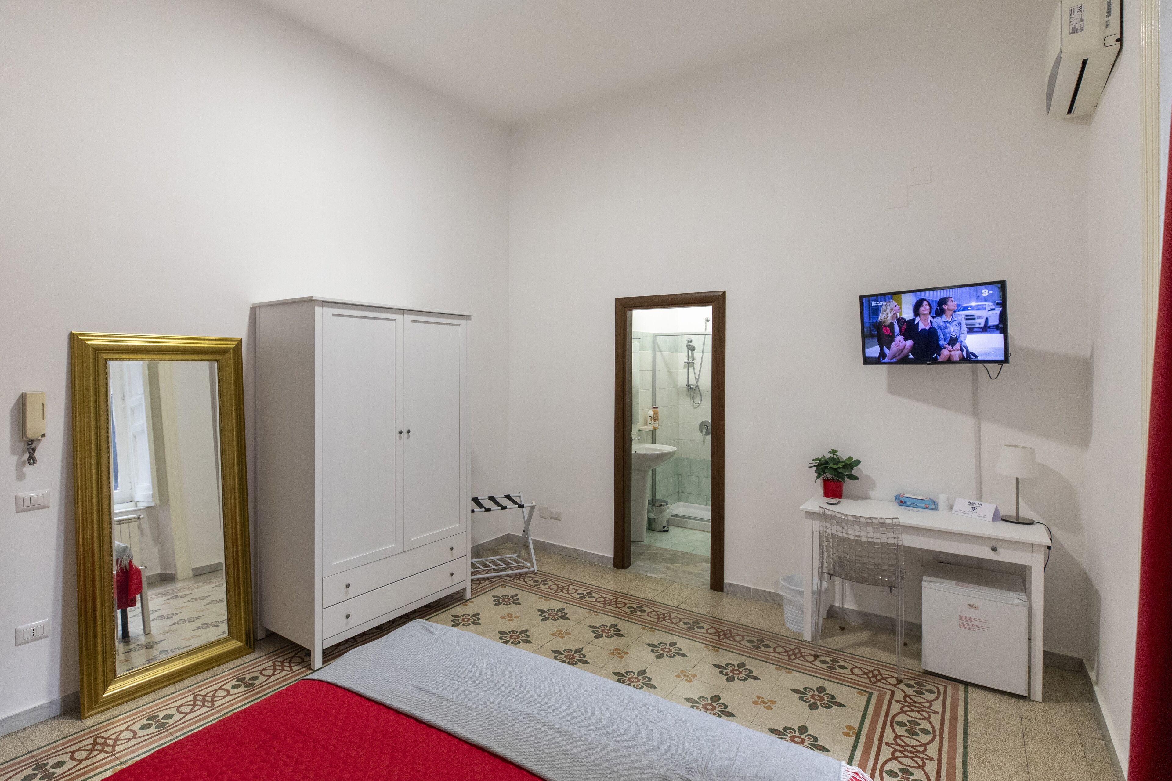 A hotel room with a bed, wardrobe, desk, TV, and a bathroom visible through an open door.