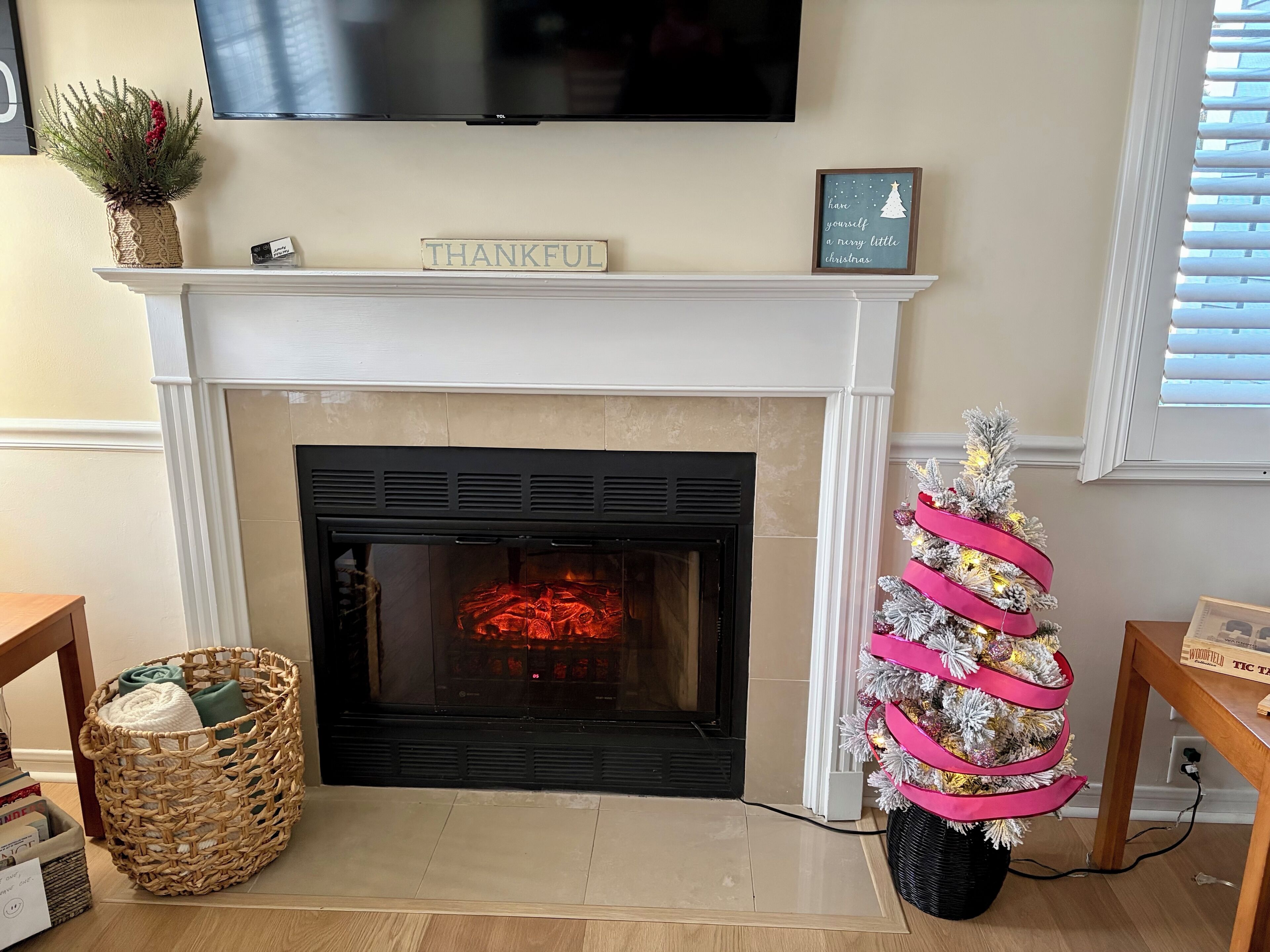 A fireplace with a 'THANKFUL' sign, a small Christmas tree, and a flat-screen TV mounted above.