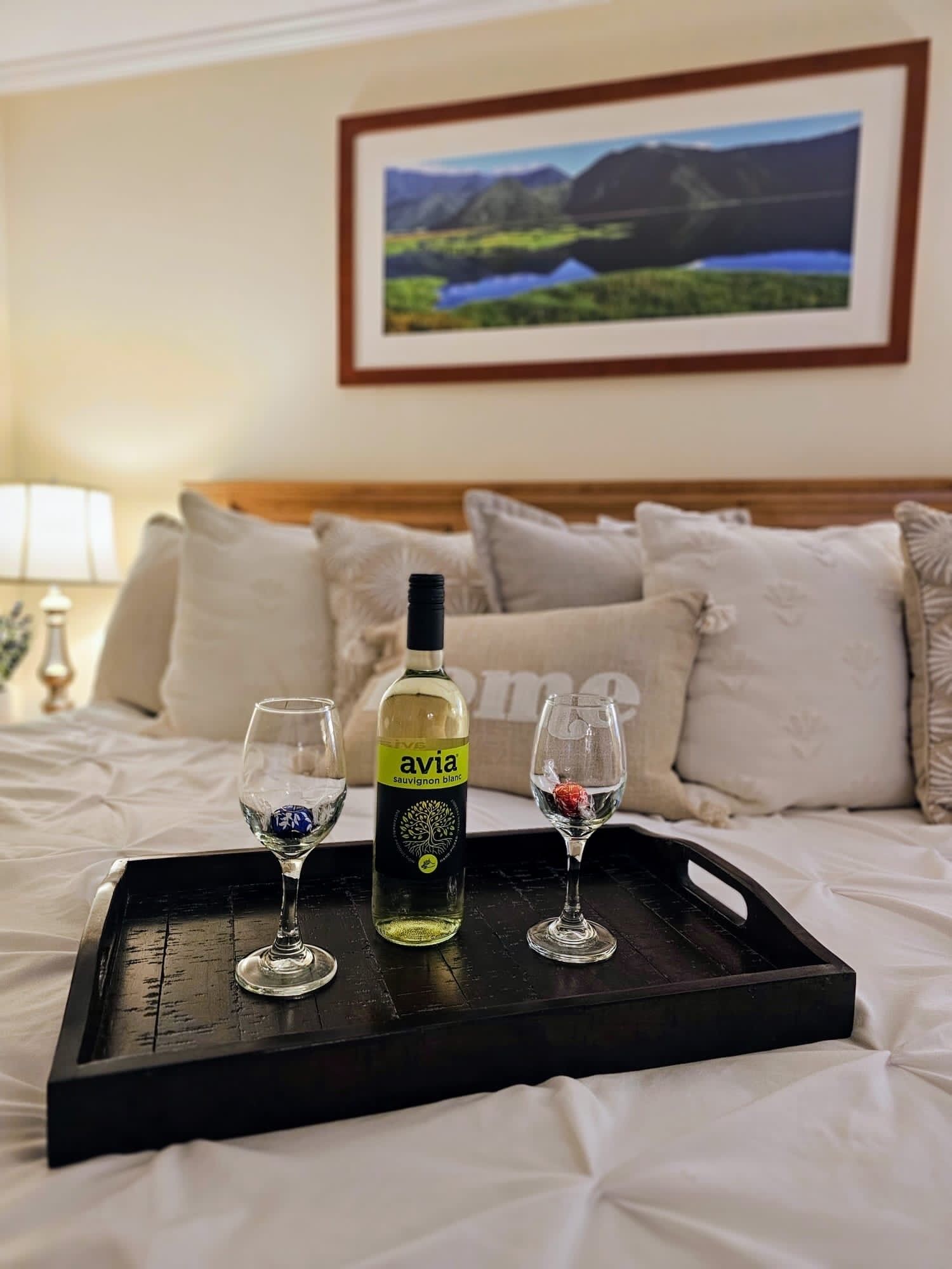 Une table de chevet sur laquelle se trouve un plateau avec une bouteille de sauvignon blanc, deux verres et une petite boîte de chocolats.