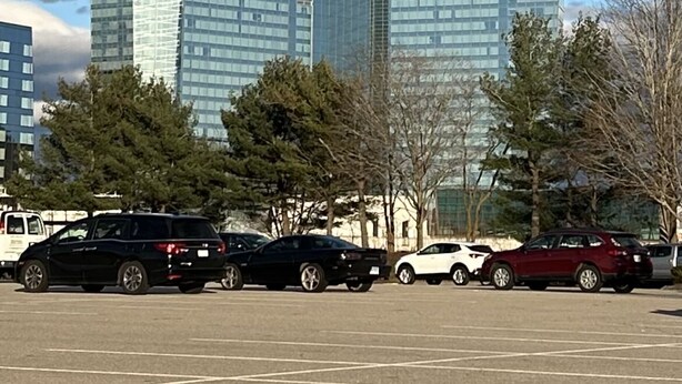 Ein Parkplatz mit mehreren Autos und einem modernen Gebäude mit Glasfenstern im Hintergrund.