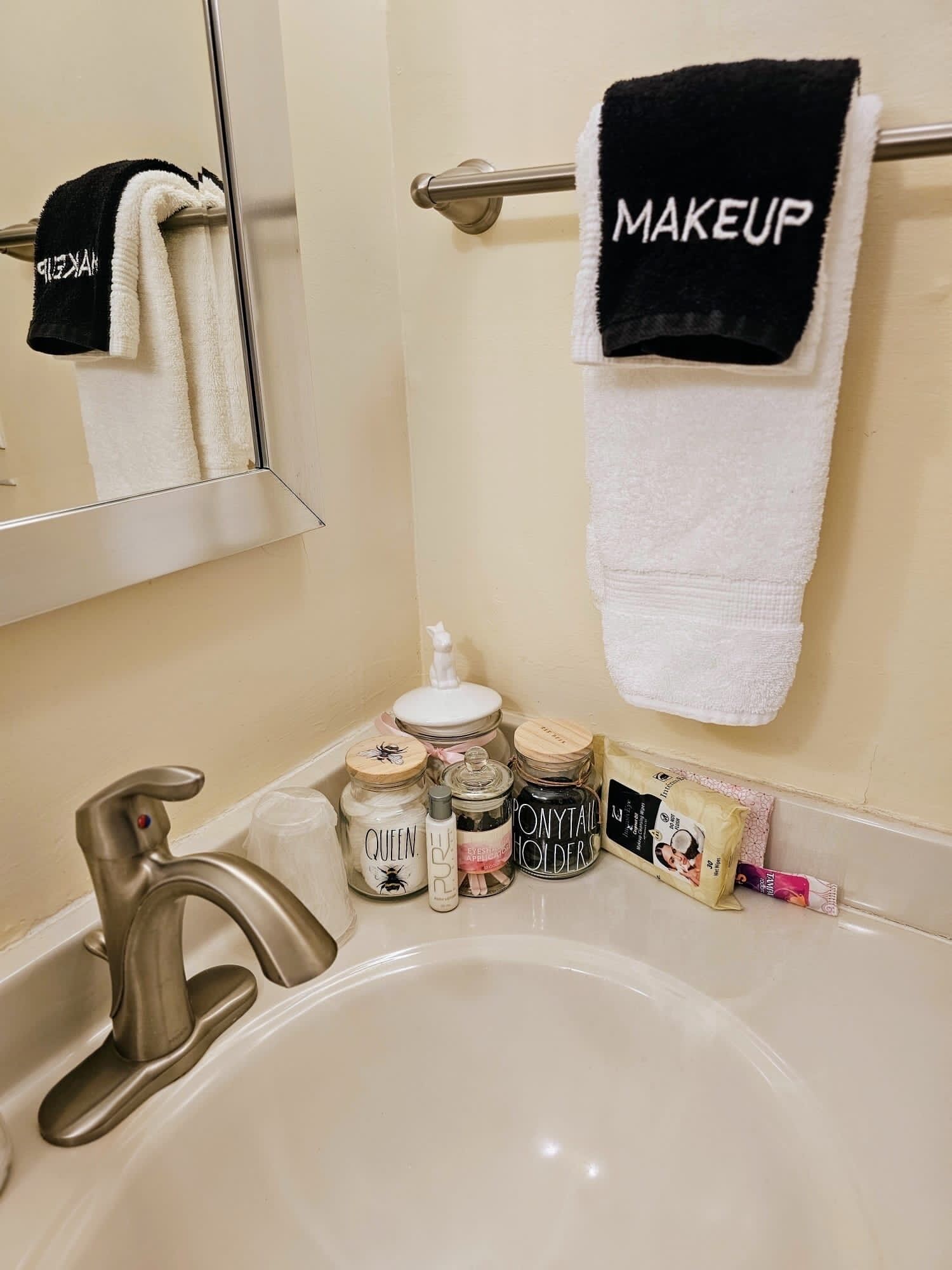 Une salle de bain avec un lavabo, un miroir et un porte-serviettes sur lequel est posée une serviette étiquetée « MAQUILLAGE ».