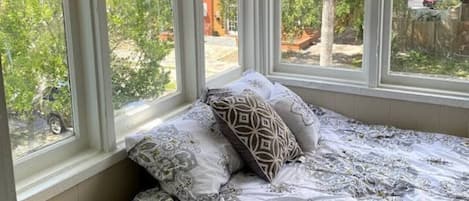 A bedroom with a bed, pillows, a wooden bench, and large windows with blinds.