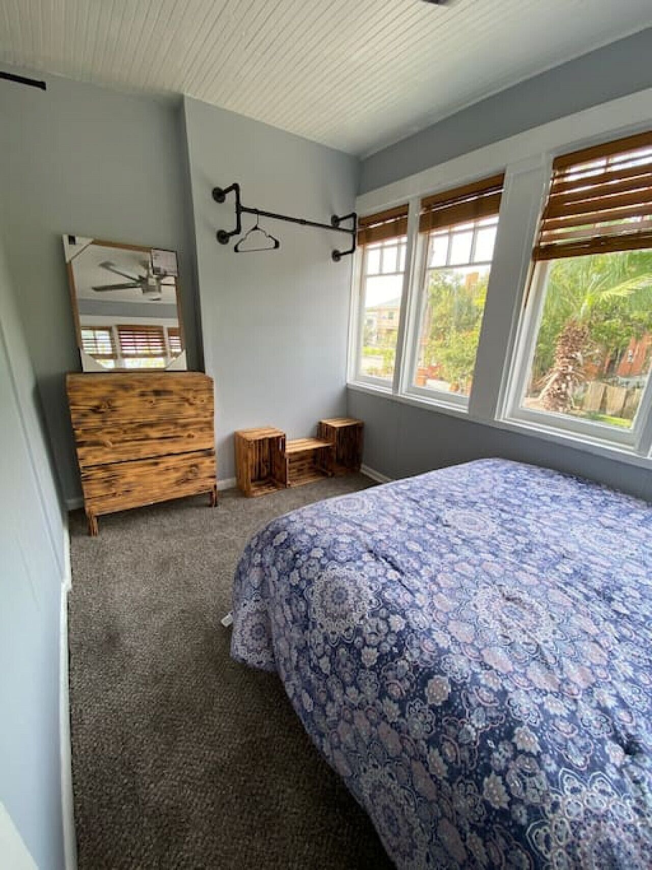 Un dormitorio con cama, cómoda, espejo, ventana con persianas y ventilador de techo.
