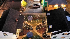 Vue aérienne d’un quartier résidentiel avec une cour centrale agrémentée d’une terrasse en bois, d’un parasol bleu et de guirlandes lumineuses.