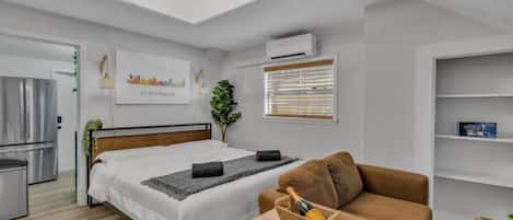 Ein modernes Hotelzimmer mit Bett, Sofa, kleinem Tisch, Pflanze und Stadtbild.