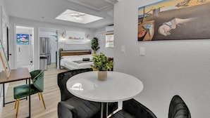 Une chambre d’hôtel moderne comprenant un lit, un coin repas avec une table ronde, un coin cuisine et un grand tableau au mur.