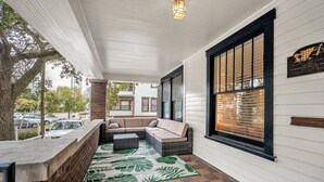 A covered porch with a seating area, a brick wall, and a large window with blinds. - 436 WHOLE PROPERTY · Downtown Historic District Estate (Home + Cottage) (St. Petersburg)