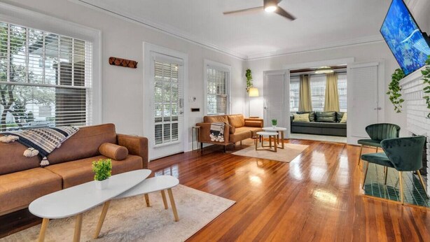 A spacious living room with hardwood flooring, a brown leather sofa, a white coffee table, and a green armchair. - 436 WHOLE PROPERTY · Downtown Historic District Estate (Home + Cottage) (St. Petersburg)