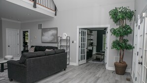 Ein geräumiges Wohnzimmer mit grauem Sofa, einer großen Kühlpflanze und einer Treppe, die zu einer oberen Ebene führt.